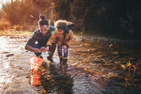 Father and son fishing with fishing net in river Young dad teaching son how to fish with fishing net in mountain stream at sunset